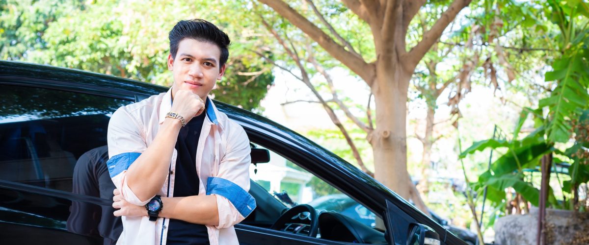 Portrait young handsome man posed standing with black car in park, he looking and smiling to camera
